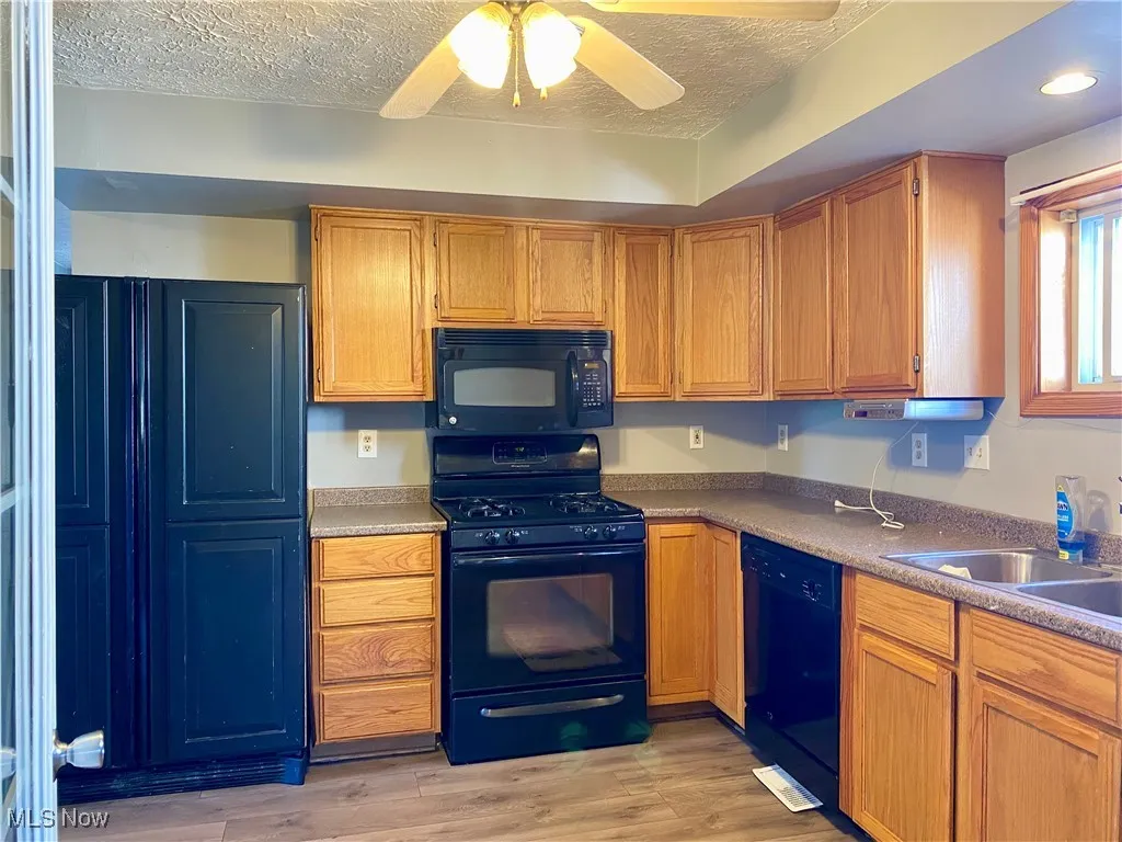 Kitchen featuring black appliances, light wood-style flooring, brown cabinets, a textured ceiling, and a ceiling fan