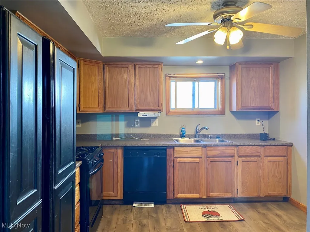 Kitchen with dark countertops, black appliances, brown cabinetry, a textured ceiling, and dark wood-style floors