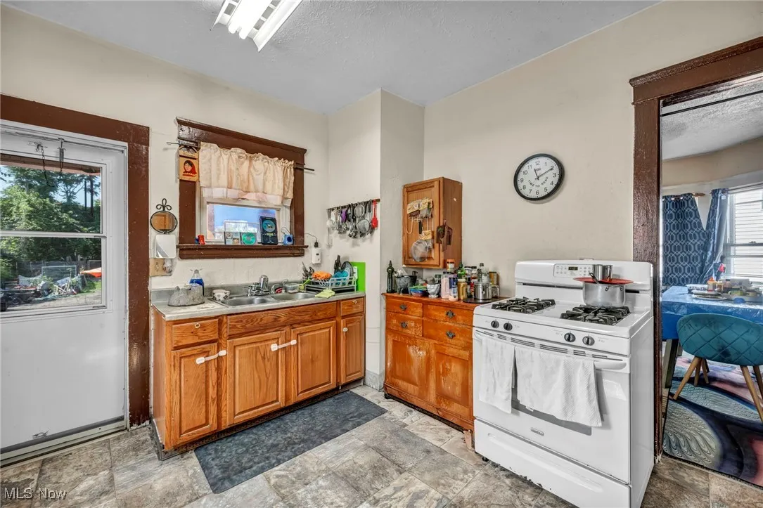 Kitchen with gas range gas stove, brown cabinetry, light countertops, a textured ceiling, and stone finish flooring