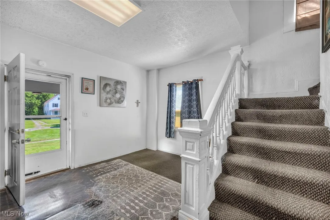 Carpeted foyer featuring a textured ceiling, plenty of natural light, and stairs