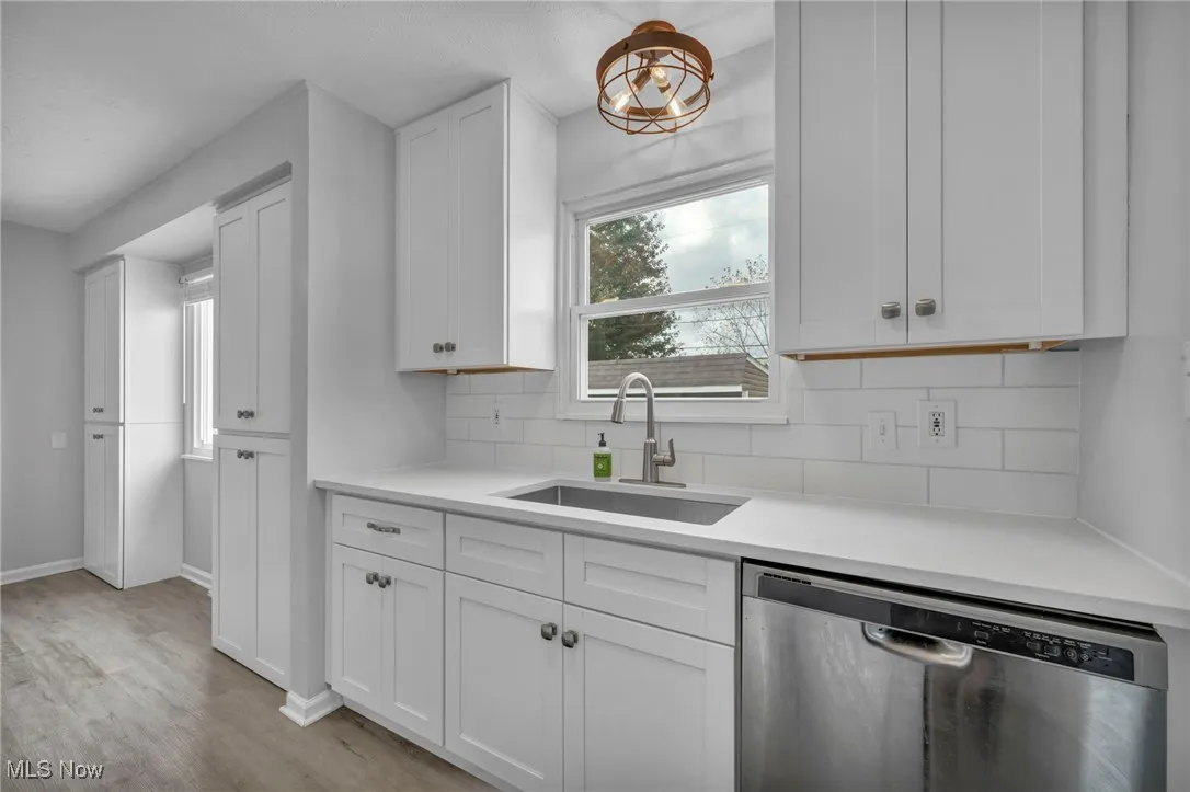 Kitchen featuring stainless steel dishwasher, tasteful backsplash, white cabinets, light wood-type flooring, and light stone countertops