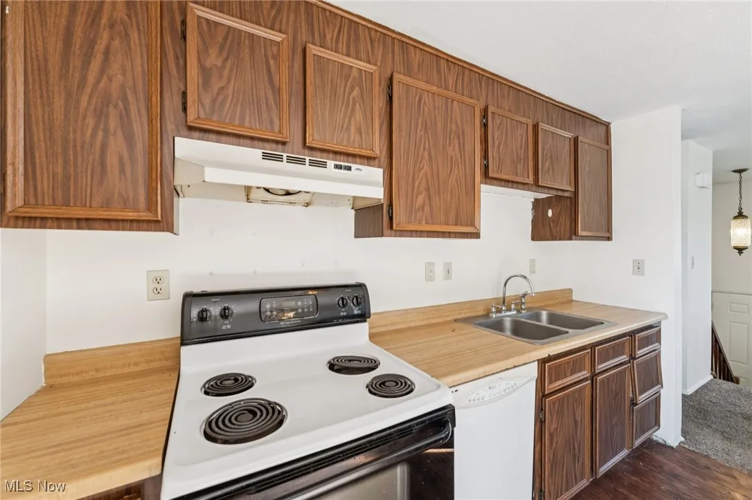 Kitchen with white appliances, light countertops, under cabinet range hood, and brown cabinetry