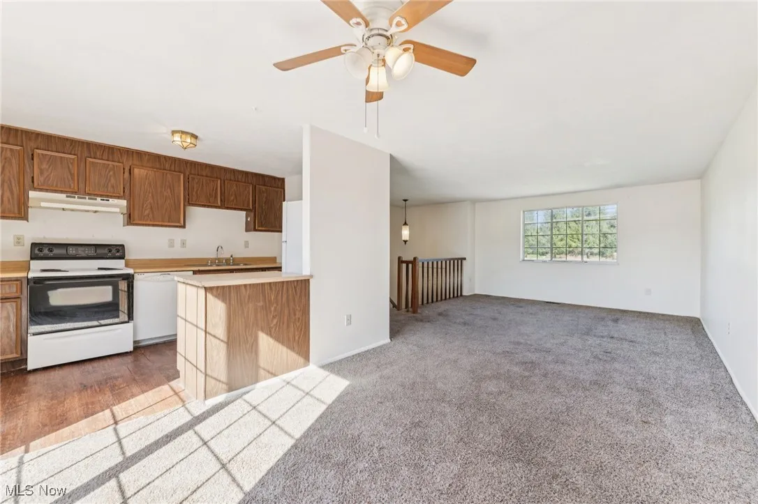 Kitchen featuring white appliances, light countertops, open floor plan, light colored carpet, and under cabinet range hood