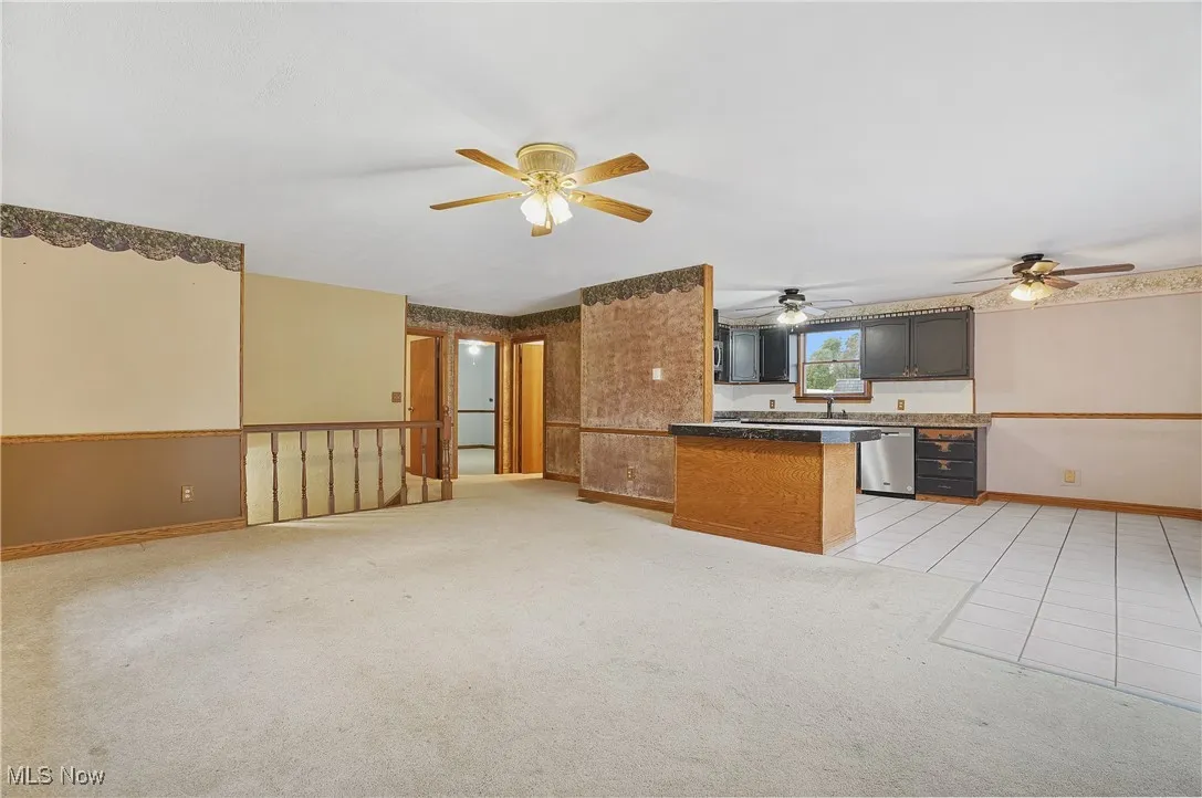 Kitchen featuring dark countertops, light colored carpet, light tile patterned floors, stainless steel dishwasher, and open floor plan