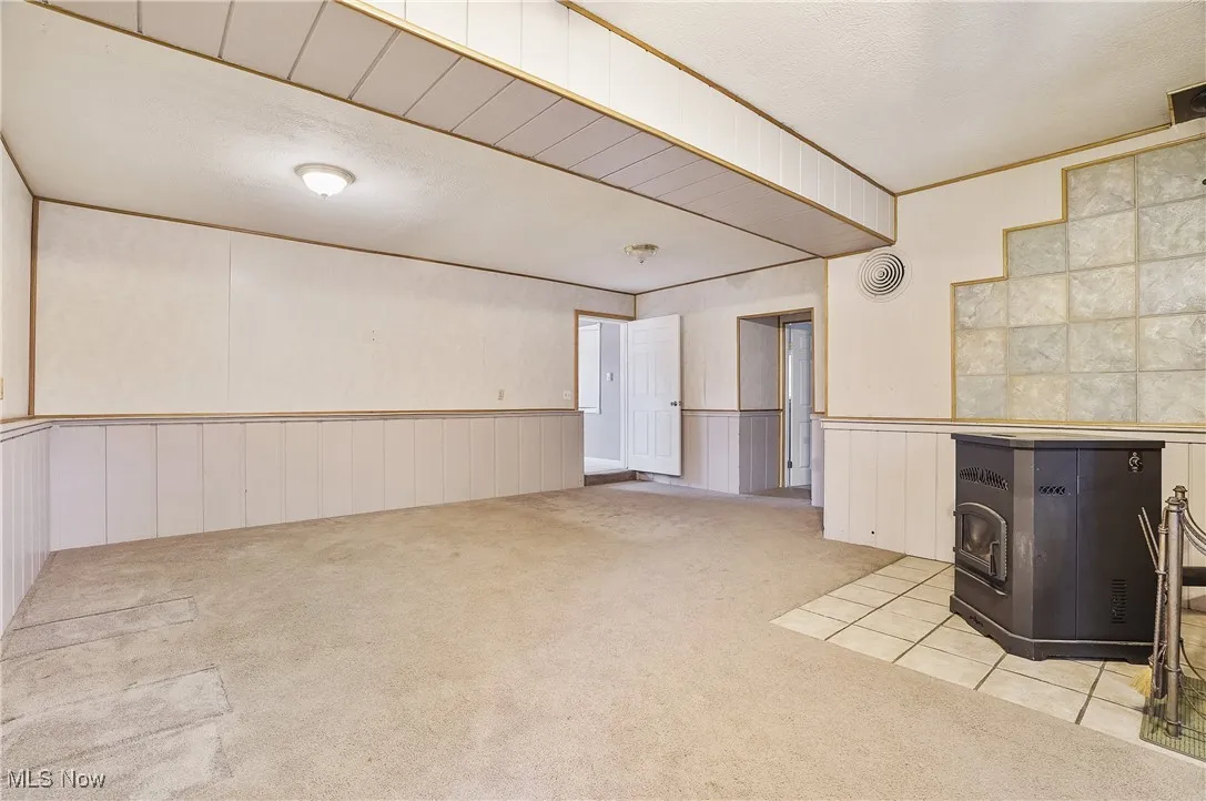 Unfurnished living room featuring carpet, a wood stove, a textured ceiling, crown molding, and a wainscoted wall