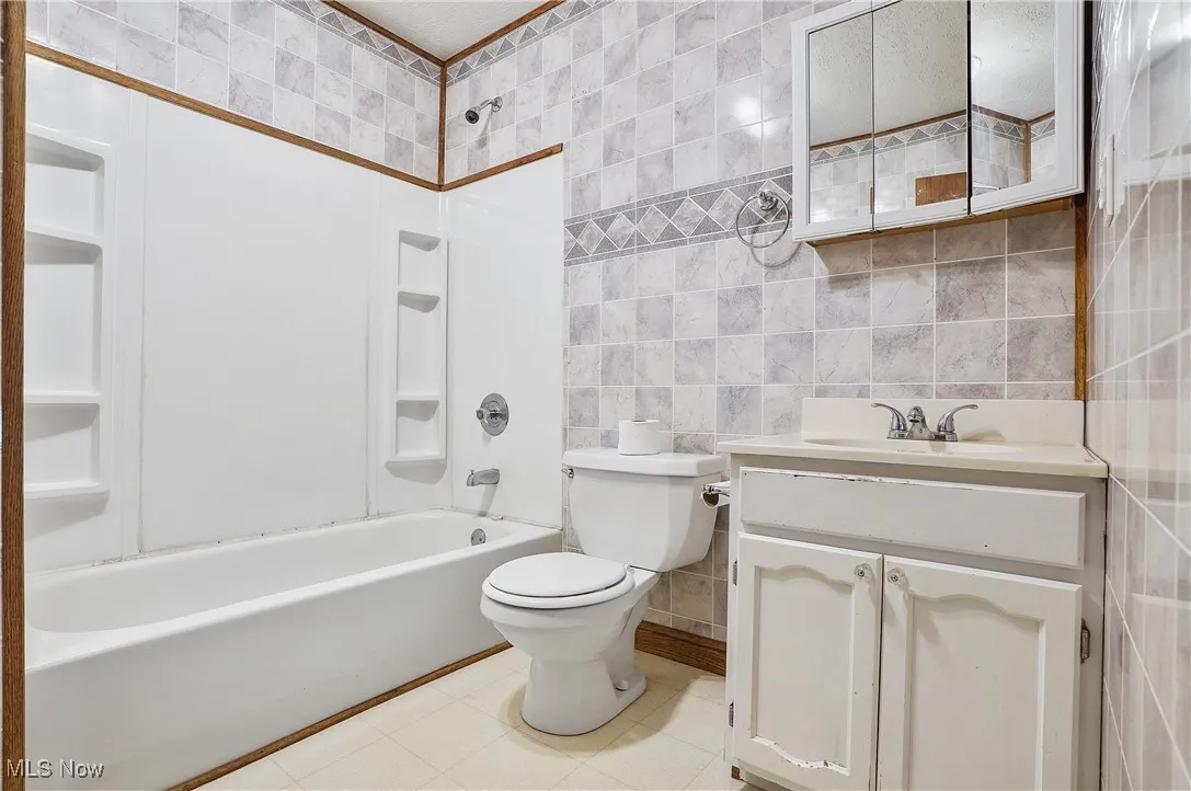 Full bath with tile walls, bathtub / shower combination, and vanity