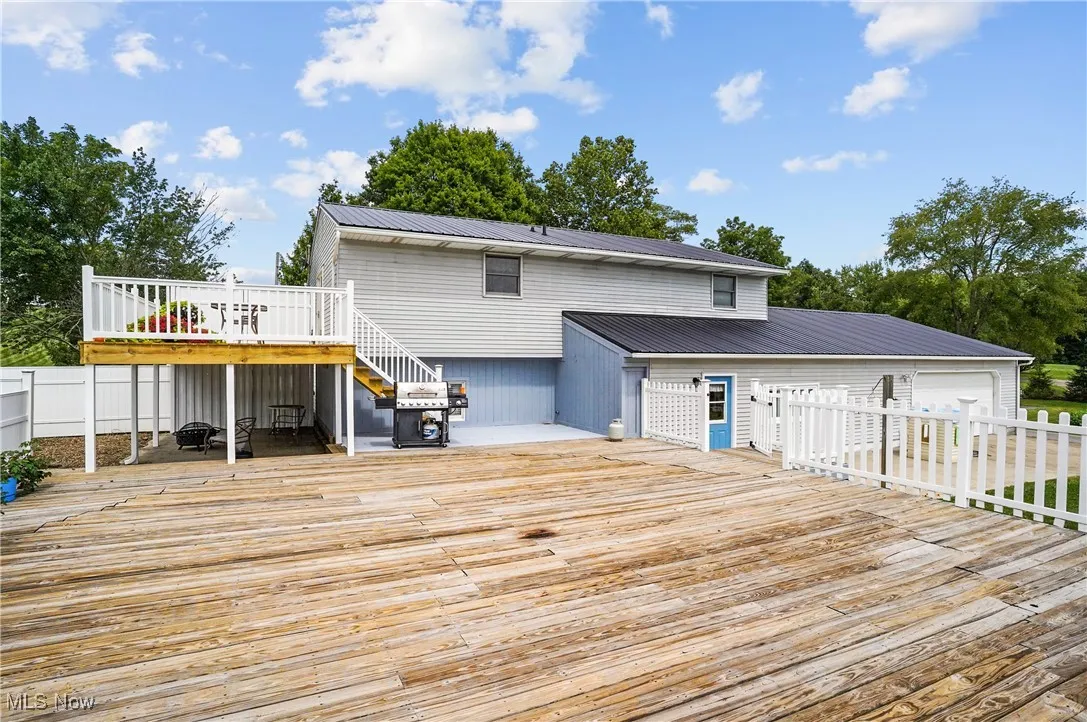 Back of property with a wooden deck, stairway, a metal roof, and a garage