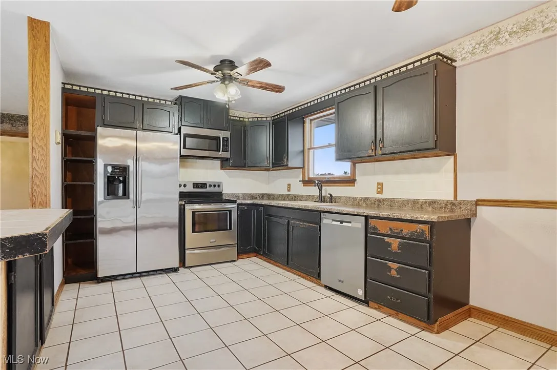 Kitchen featuring appliances with stainless steel finishes, light tile patterned floors, a ceiling fan, and tile counters