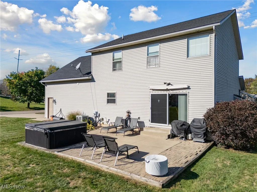 Back of property with a yard, a patio area, a hot tub, and a shingled roof