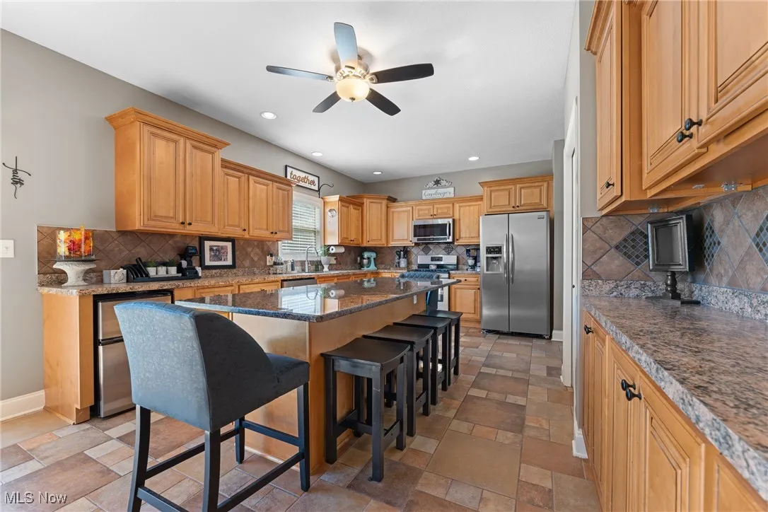 Kitchen featuring stainless steel appliances, backsplash, a breakfast bar area, recessed lighting, and stone tile floors