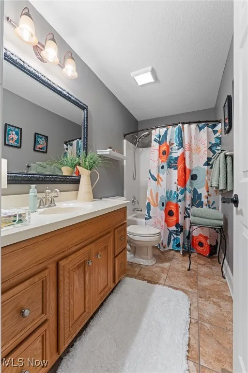 Full bathroom with vanity, shower / bathtub combination with curtain, a textured  and  tile patterned floors