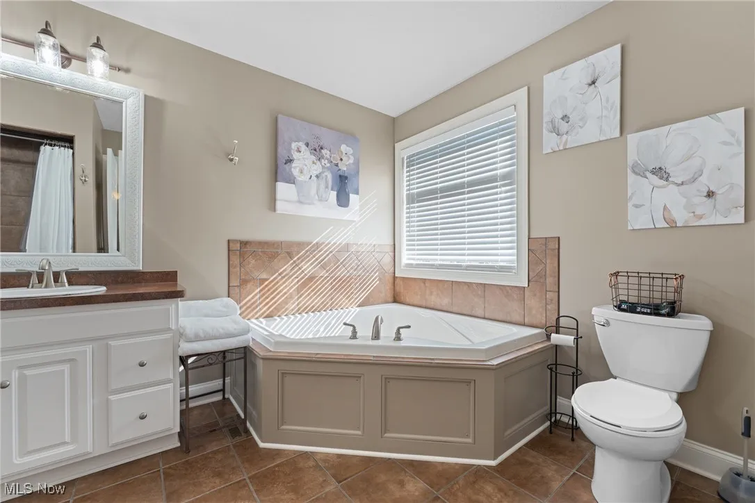 Bathroom featuring vanity, a garden tub, dark tile patterned floors, and curtained shower