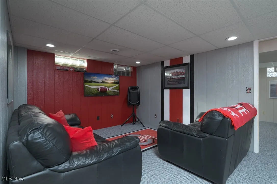 Carpeted living room featuring a drop ceiling, wood walls, and recessed lighting