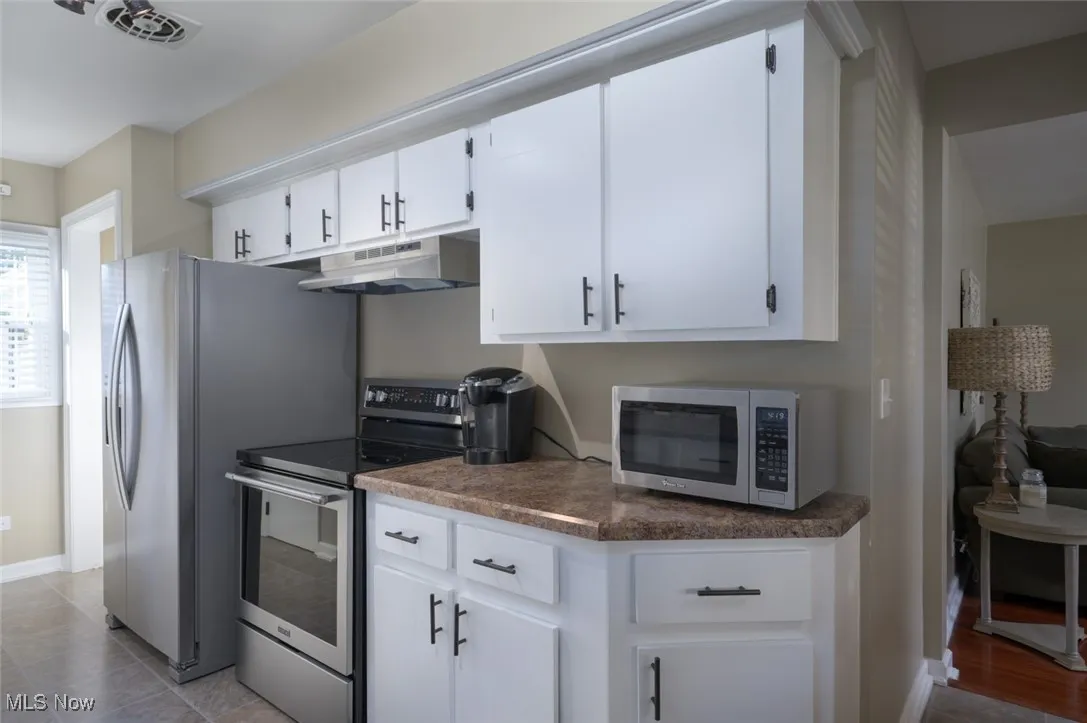 Kitchen with appliances with stainless steel finishes, under cabinet range hood, and white cabinets
