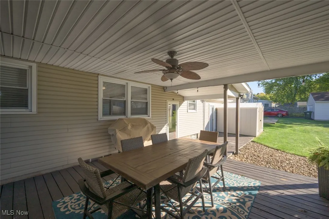 Wooden terrace featuring a ceiling fan, outdoor dining area, a grill, and a storage unit