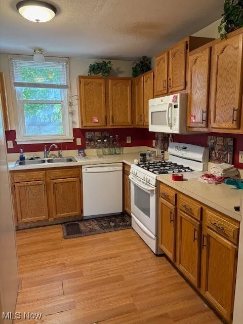 Kitchen with white appliances, brown cabinetry, light countertops, light wood-style flooring, and a textured ceiling