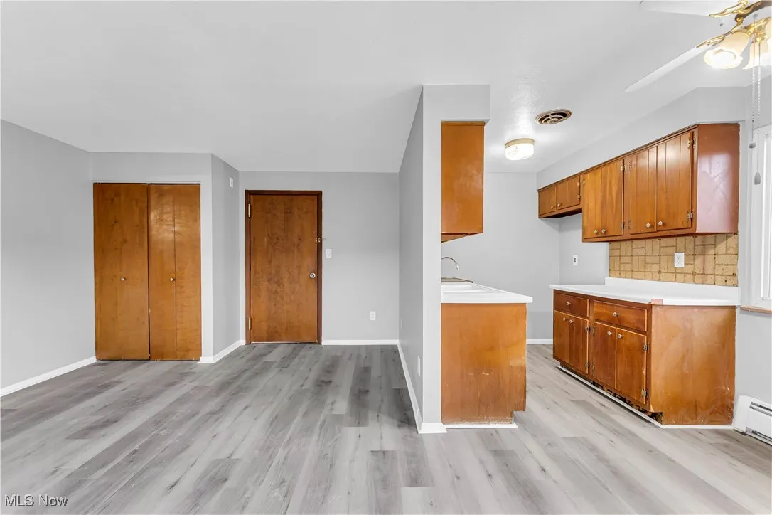 Kitchen featuring light countertops, ceiling fan, light wood-type flooring, brown cabinets, and tasteful backsplash
