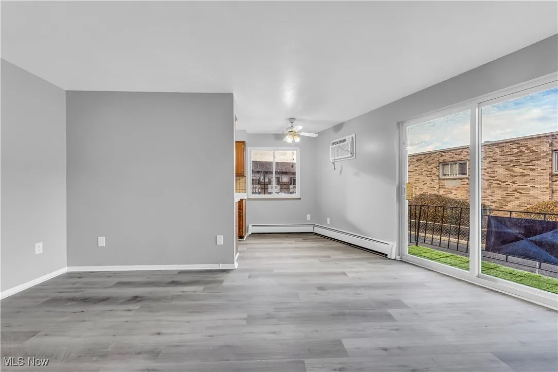 Empty room featuring light wood-style floors, a ceiling fan, a wall unit AC, and a baseboard radiator