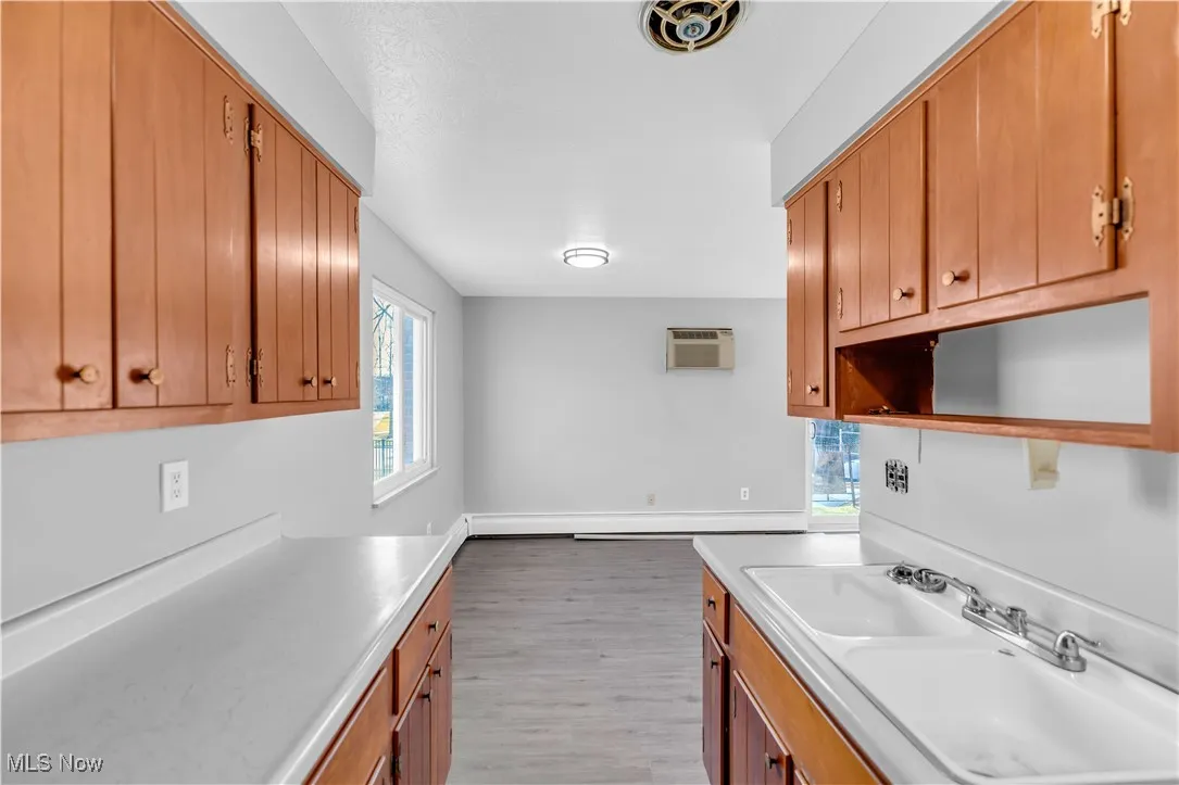 Kitchen with light countertops, brown cabinetry, light wood-type flooring, open shelves, and an AC wall unit