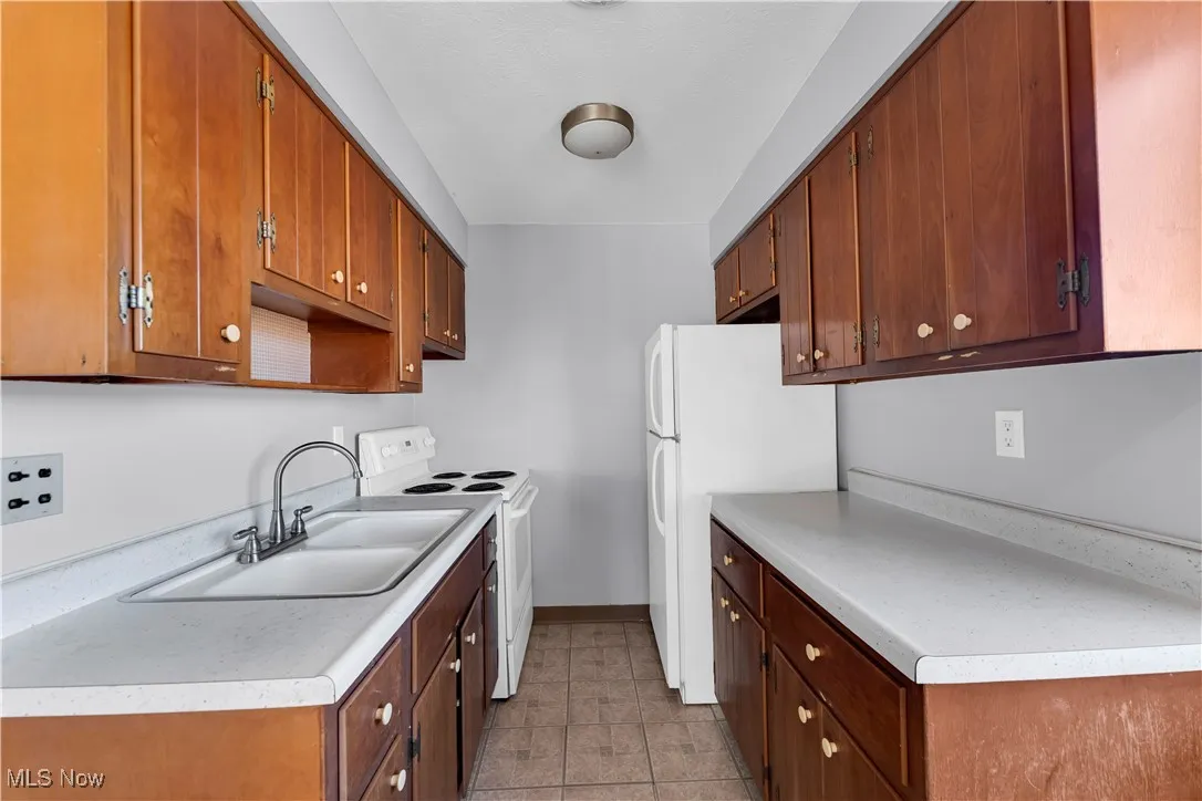 Kitchen featuring white appliances, light countertops, light tile patterned floors, and brown cabinets