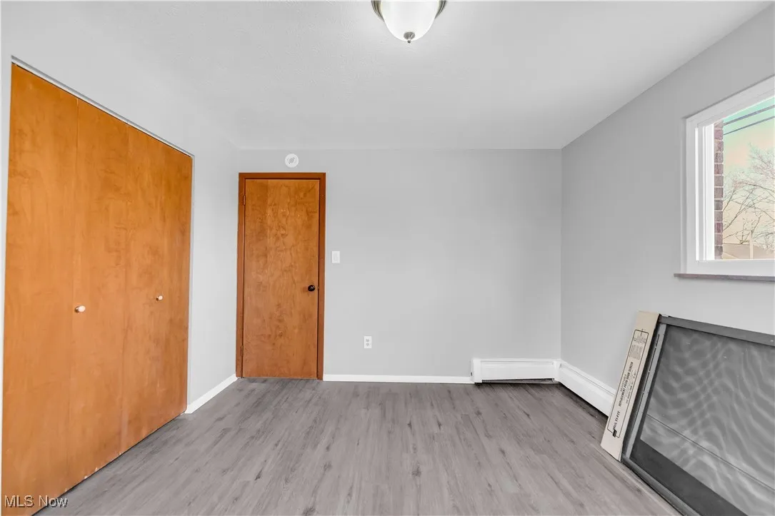 Unfurnished bedroom featuring light wood-style floors, a closet, and a baseboard heating unit