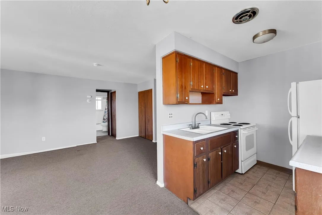 Kitchen featuring white appliances, light countertops, brown cabinetry, and light colored carpet
