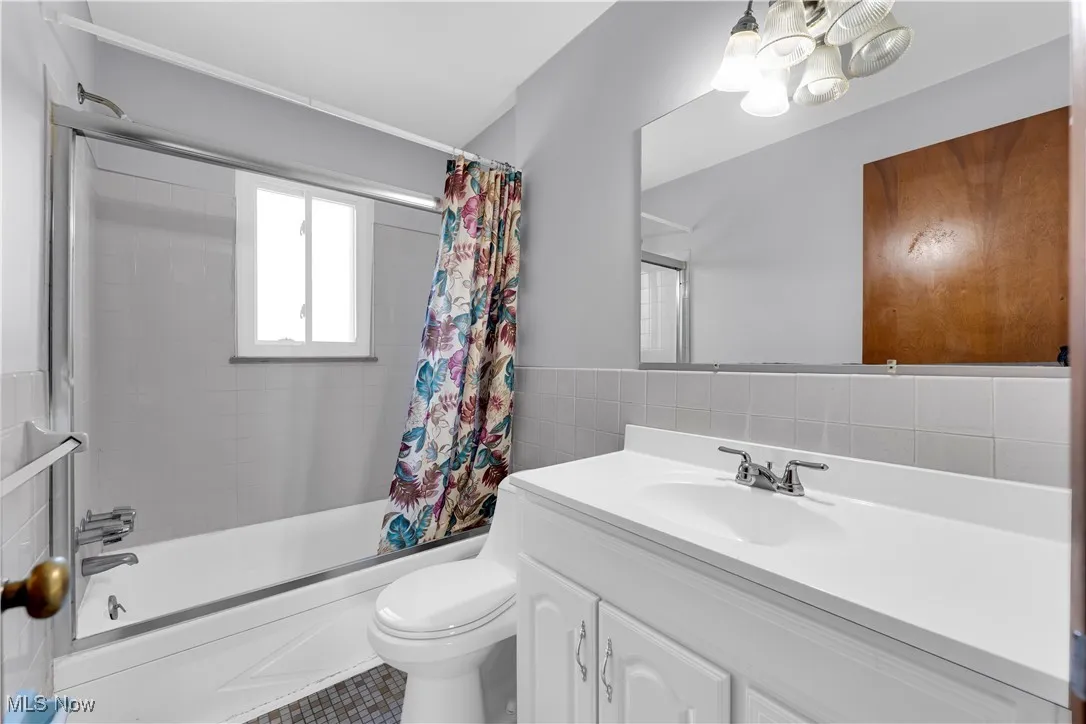 Bathroom featuring shower / bath combo with shower curtain, tile walls, vanity, a chandelier, and wainscoting
