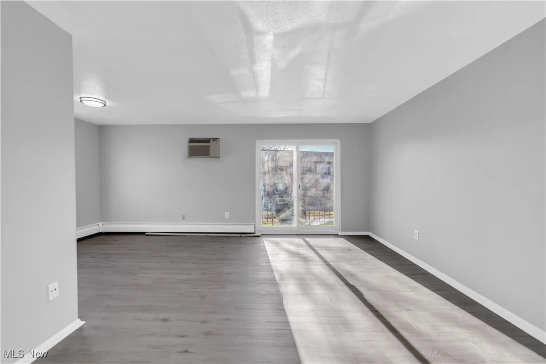 Spare room featuring wood finished floors, a wall unit AC, and baseboard heating