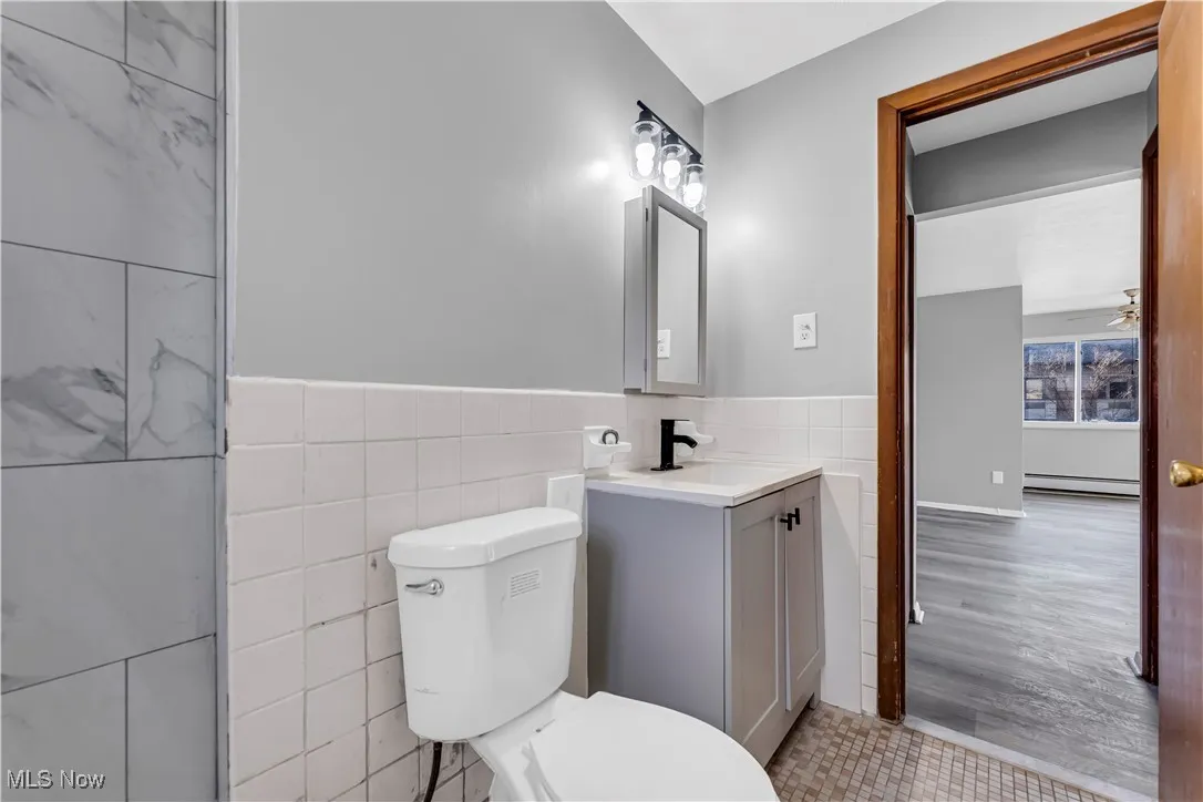 Bathroom featuring vanity, tile walls, a ceiling fan, a wainscoted wall, and a baseboard radiator