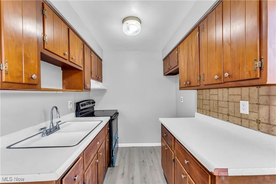 Kitchen with black range with electric stovetop, brown cabinetry, and light wood-type flooring