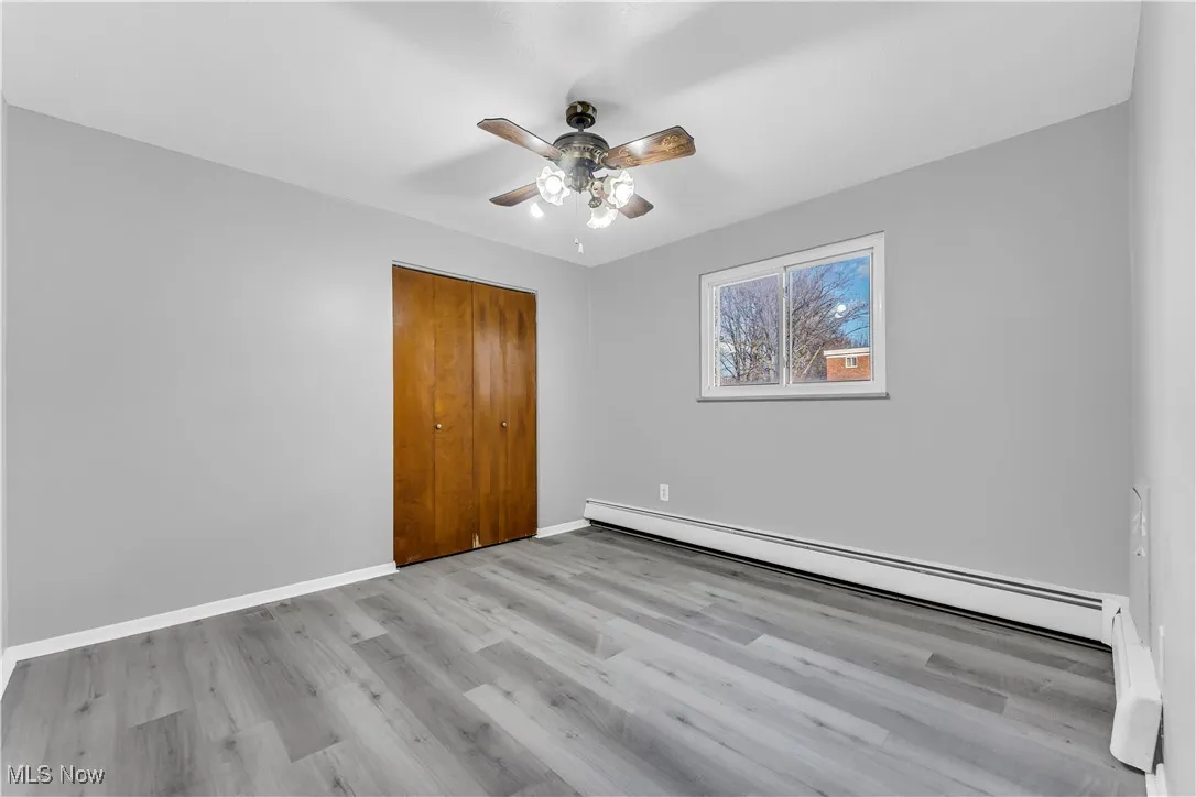 Unfurnished bedroom featuring a baseboard radiator, light wood-type flooring, a ceiling fan, and a closet