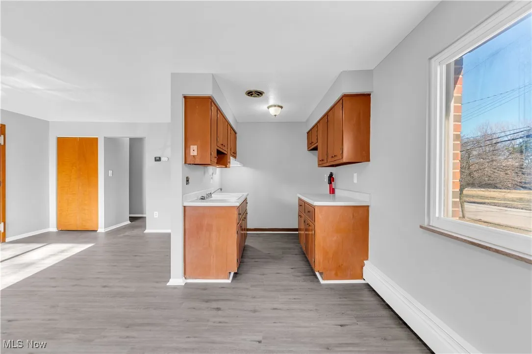 Kitchen featuring light countertops, light wood-style floors, a baseboard radiator, and brown cabinetry