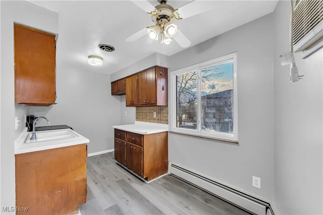 Kitchen with a baseboard heating unit, light countertops, light wood-type flooring, brown cabinetry, and decorative backsplash