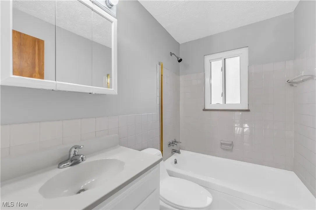 Full bathroom featuring shower / washtub combination, vanity, a textured ceiling, and tile walls