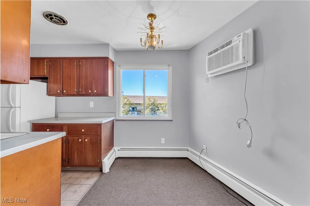 Kitchen featuring light countertops, freestanding refrigerator, a baseboard radiator, light tile patterned floors, and an AC wall unit