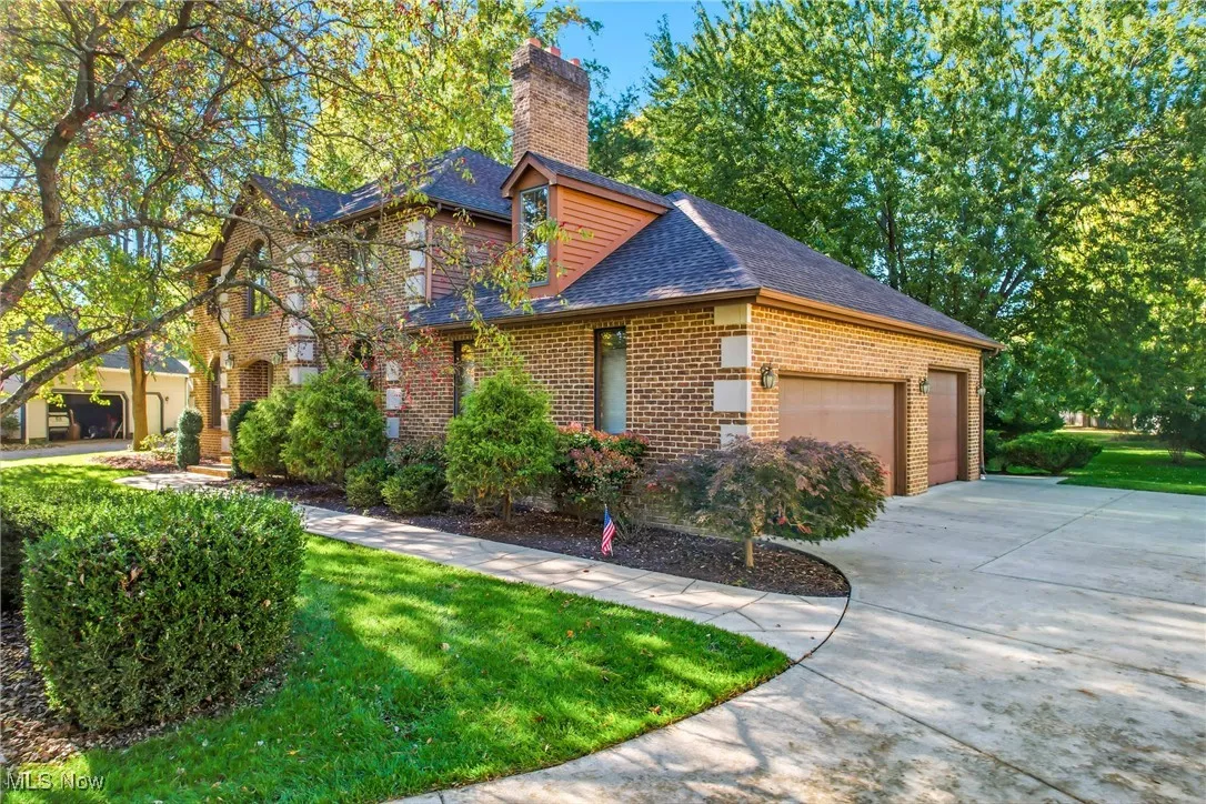 View of front facade with brick siding, roof with shingles, an attached garage, a front yard, and driveway