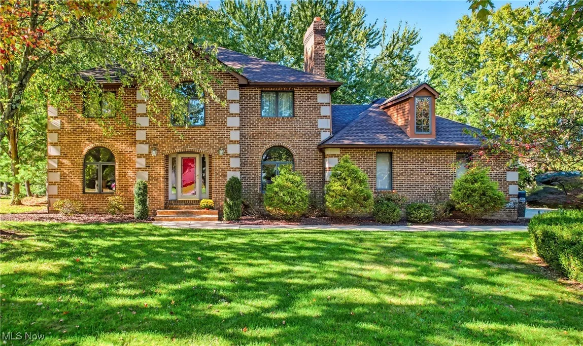 View of front of house featuring a front lawn, brick siding, a shingled roof, and a chimney