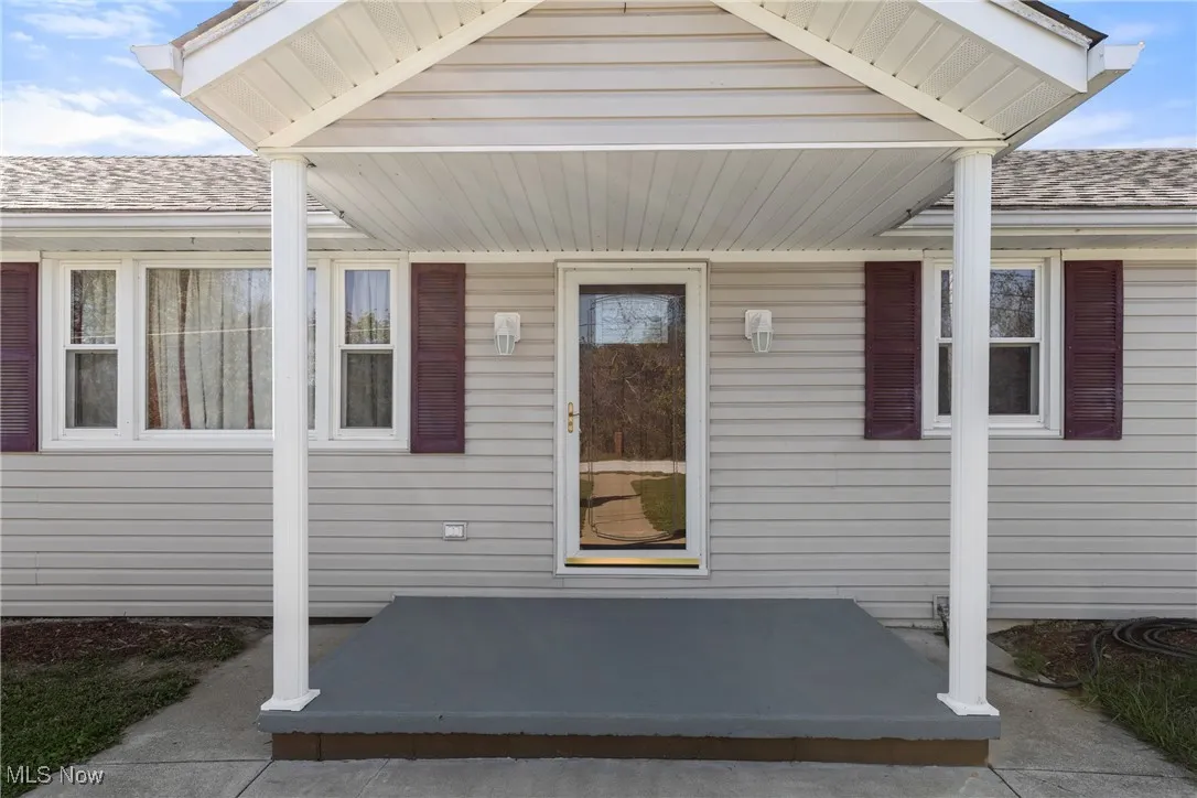 View of exterior entry featuring a shingled roof and covered porch