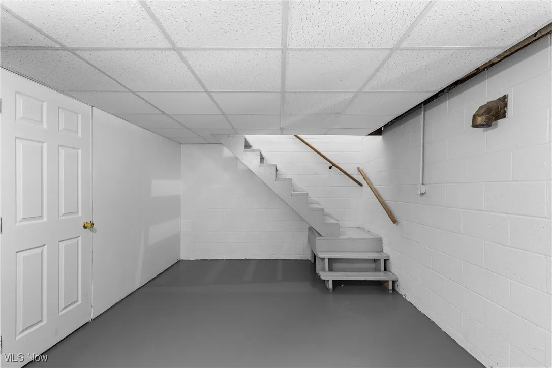 Finished below grade area with concrete block wall, a paneled ceiling, and stairway