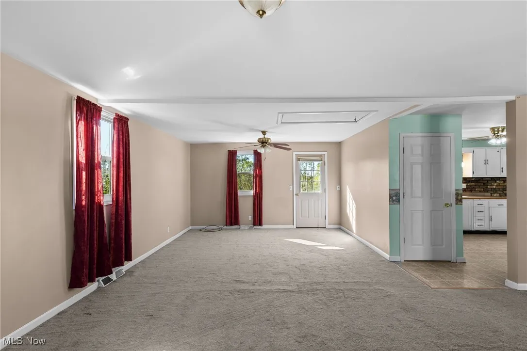 Unfurnished room featuring a ceiling fan, carpet flooring, and attic access