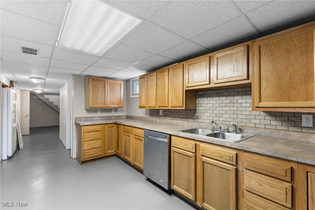 Kitchen with concrete flooring, light countertops, dishwasher, decorative backsplash, and white refrigerator with ice dispenser