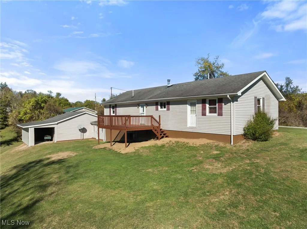 Back of property with a yard, a deck, stairs, an outbuilding, and a shingled roof