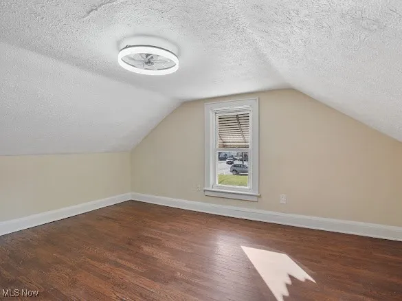 Additional living space with a textured ceiling, dark wood finished floors, and lofted ceiling