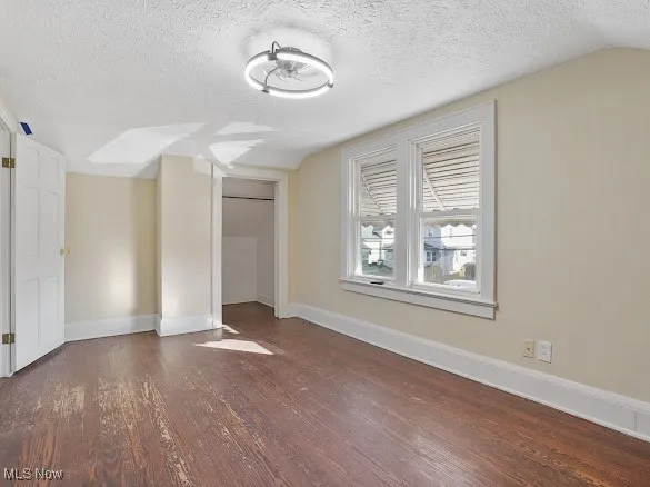 Unfurnished bedroom with a textured ceiling, dark wood finished floors, vaulted ceiling, and a closet