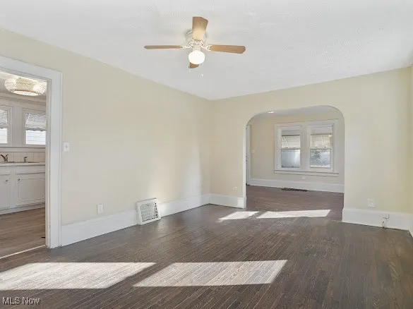 Unfurnished room with dark wood-style flooring, plenty of natural light, a ceiling fan, and arched walkways