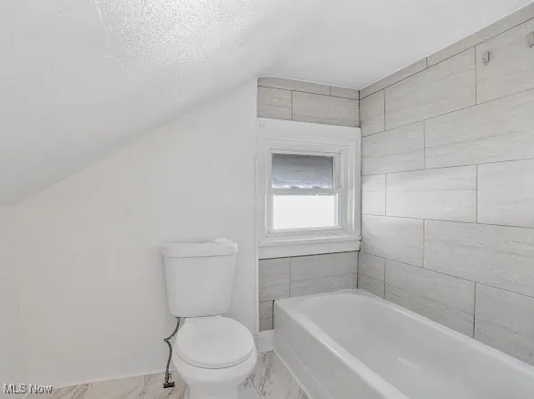 Full bath with lofted ceiling, a bath, and a textured ceiling