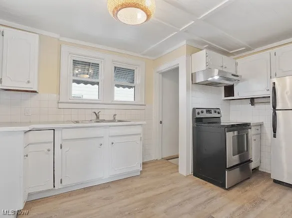 Kitchen with appliances with stainless steel finishes, white cabinets, light wood finished floors, light countertops, and under cabinet range hood