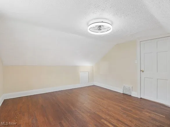 Additional living space with vaulted ceiling, a textured ceiling, and dark wood-style floors