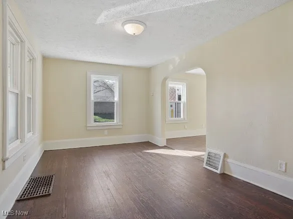Spare room featuring dark wood finished floors, a textured ceiling, and arched walkways