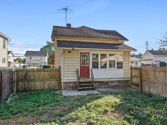 Back of house with entry steps, a fenced backyard, a chimney, and roof with shingles